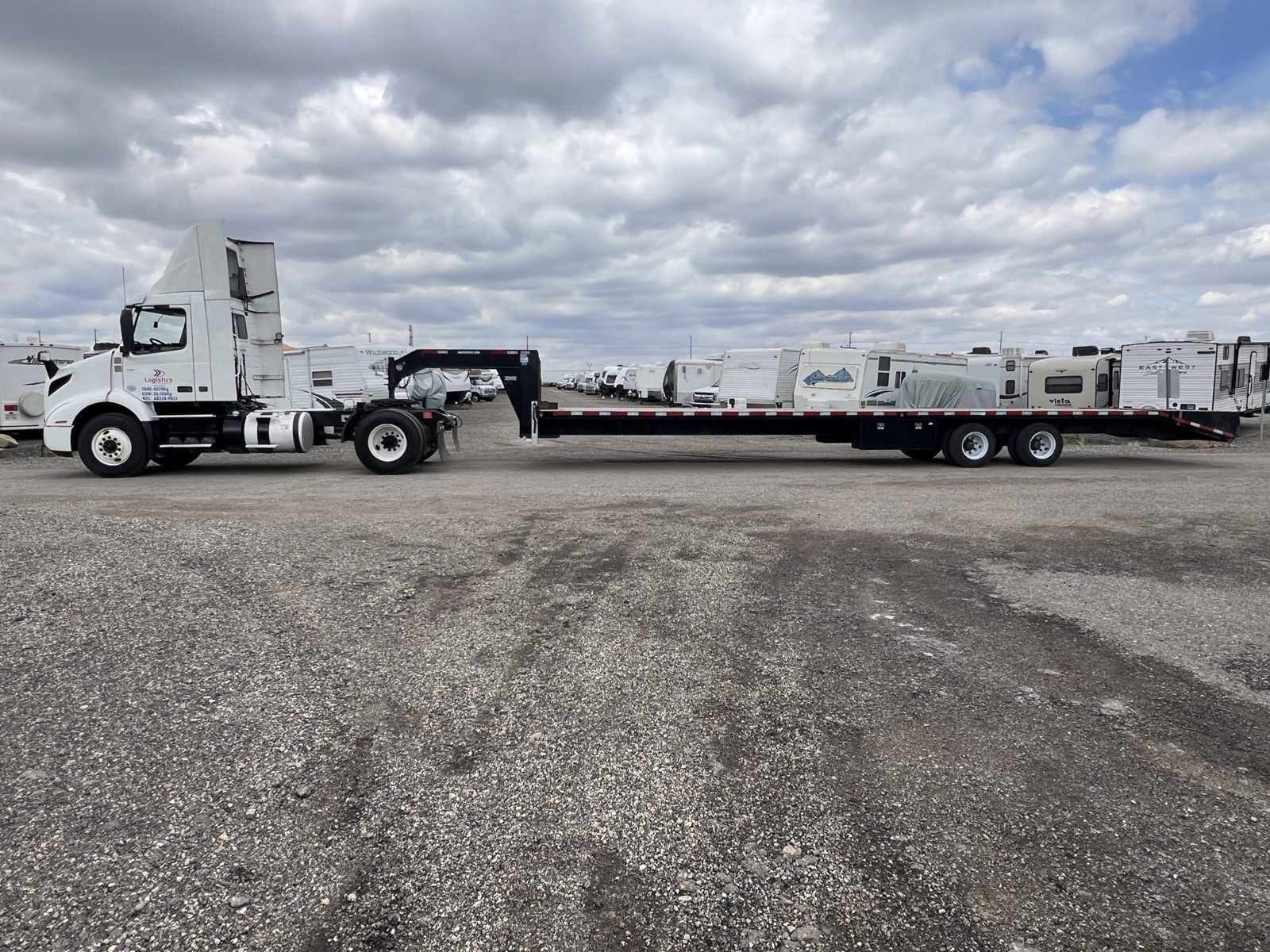 White day-cab tractor with a long flatbed trailer