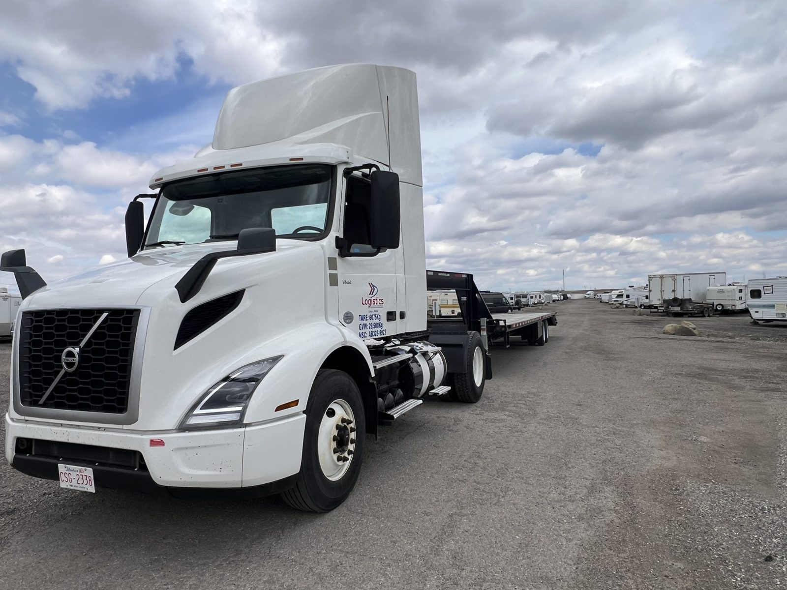 White Volvo day-cab tractor with flatbed trailer